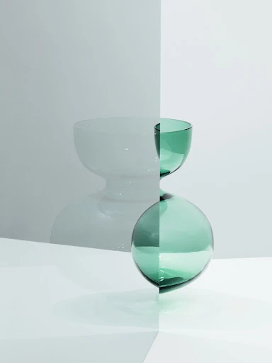 Minimalist still life with a green glass bowl stacked on a green glass sphere, set against a two-tone gray and white backdrop.