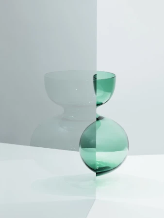 Minimalist still life with a green glass bowl stacked on a green glass sphere, set against a two-tone gray and white backdrop.