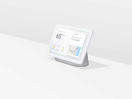 Smart home display device showcasing weather and commute information on a minimalist white surface in a brightly lit interior setting.