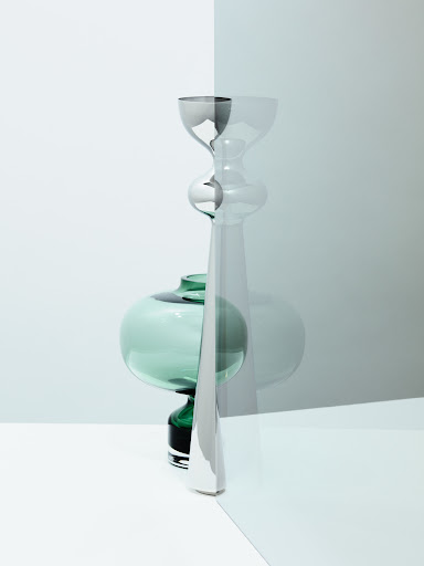 Still life studio photograph of two vases, one teal sphere and one transparent fluted vase, on a white surface against a split white and light-blue background.