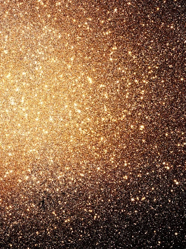 Abstract close-up of glistening, blurred, golden glitter with bokeh effect against a dark background, creating a sparkling, festive texture.
