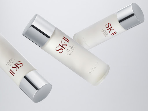 Three SK-II Facial Treatment Essence bottles with silver caps are displayed against a light gray background in a beauty product shot.