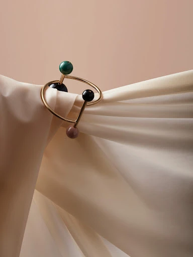 Stylish gold bracelet with three decorative beads draped over soft, draped fabric, set against a plain peach-colored backdrop.