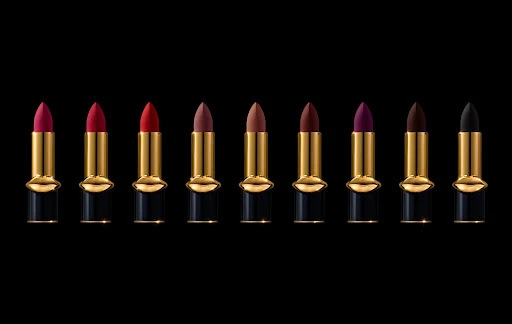 A row of lipstick tubes in varying colors with gold accents and black bases against a black background, product photography for beauty.