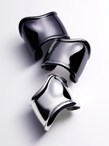 High-angle shot of three glossy cuff bracelets, stacked and staggered, in black, gray, and silver tones on a white surface.