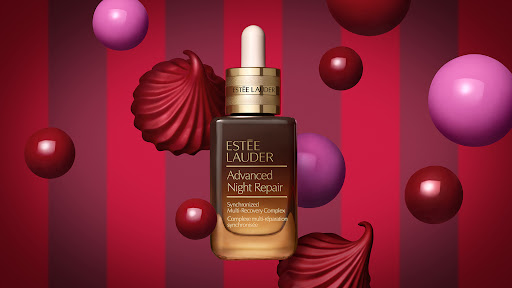 Estee Lauder Advanced Night Repair serum with a dropper, presented against a bold red and pink striped background with floating spheres.