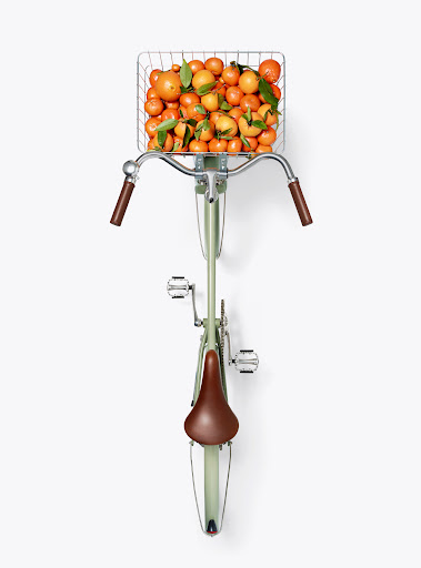 Overhead shot of a light green bicycle with a basket full of oranges, creating a vibrant and refreshing still life composition.