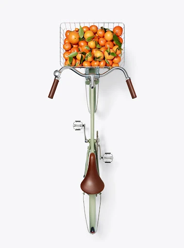 Overhead shot of a light green bicycle with a basket full of oranges, creating a vibrant and refreshing still life composition.