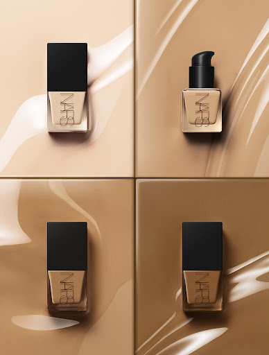 Four bottles of NARS foundation are arranged on a square tile background with beige foundation swirls for a beauty advertisement.