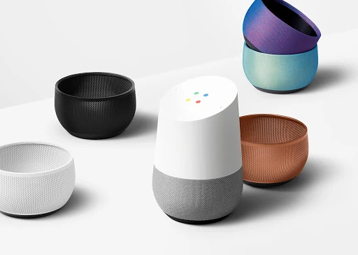 A white and grey smart speaker in the foreground surrounded by several colorful mesh accessory bases on a white background.