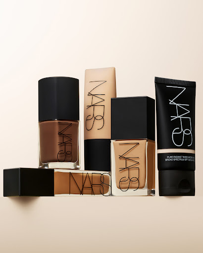 NARS makeup product group on beige background, including foundation in glass bottles and a squeeze tube with black caps and clear logo.