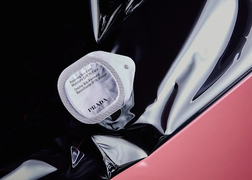 Close-up of Prada Reviving Bio-Firm Moisture SPF15/Face cream container on black, silver, and pink reflective surfaces.