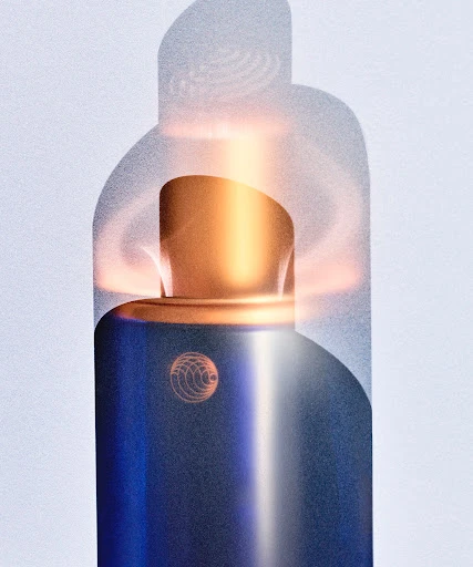 A digitally rendered product shot features a cylindrical blue and gold perfume bottle against a light background with a vaporous shadow effect.