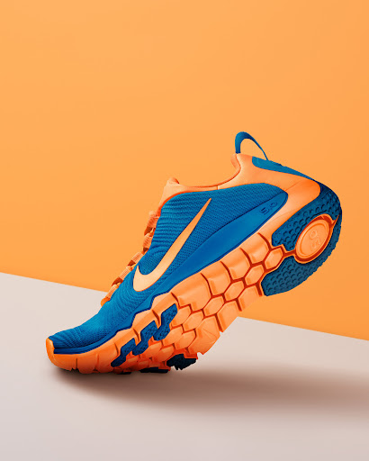 Studio shot of a blue and orange Nike running shoe. The athletic shoe is on a white surface in front of an orange background.