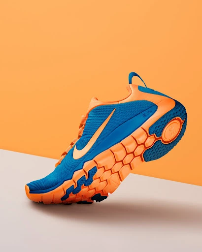 Studio shot of a blue and orange Nike running shoe. The athletic shoe is on a white surface in front of an orange background.