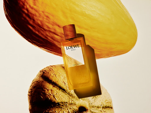 Loewe Solo fragrance bottle centered with a tan cap and yellow liquid, against sliced yellow fruit, creating a vibrant beauty composition.