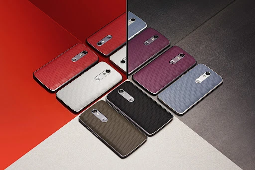 Array of smartphones in various colors including red, purple, blue, brown, white, and black arranged on a multi-tone surface.