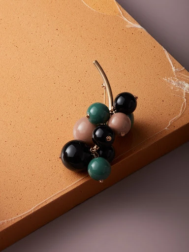 Elevated shot of a cluster brooch with green, black, and pink spheres, attached to a tan and grey backdrop.