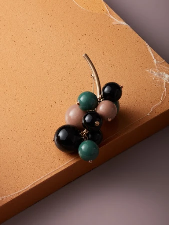 Elevated shot of a cluster brooch with green, black, and pink spheres, attached to a tan and grey backdrop.