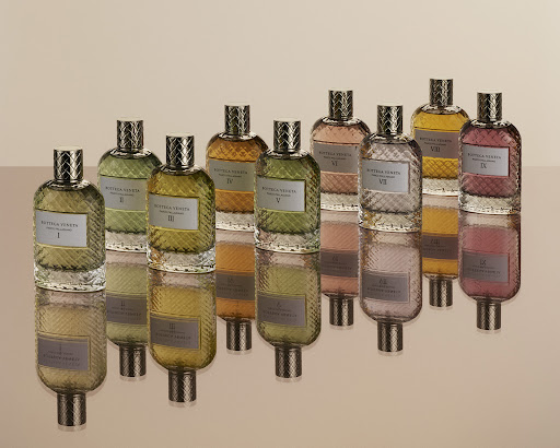 Elevated eye-level display: Ten glass perfume bottles, each filled with differently tinted liquid, are arranged on a reflective surface.