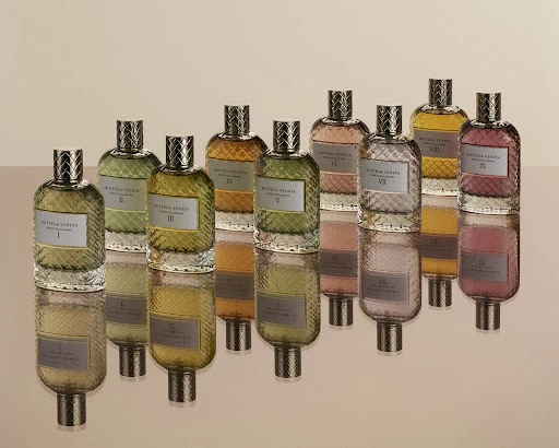 Elevated eye-level display: Ten glass perfume bottles, each filled with differently tinted liquid, are arranged on a reflective surface.
