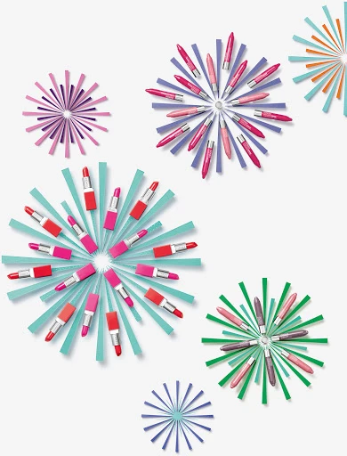 Overhead shot of colorful lipsticks arranged in starburst patterns against a white backdrop, creating a vibrant and artistic beauty product display.
