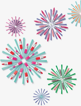 Overhead shot of colorful lipsticks arranged in starburst patterns against a white backdrop, creating a vibrant and artistic beauty product display.