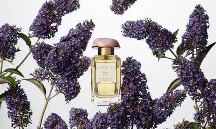 Aerin Lilac Path perfume bottle surrounded by blooming purple butterfly bush flowers on a clean white background.