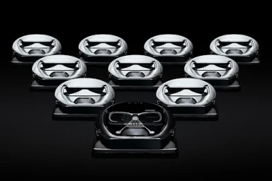 Ten robotic vacuums arranged in a triangular formation against a solid black background, with one Darth Vader themed vacuum at the front