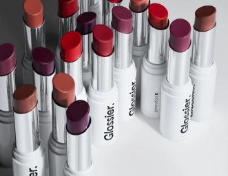 A close-up shot of multiple Glossier lipstick tubes with varied colored tips arranged on a clean white background.