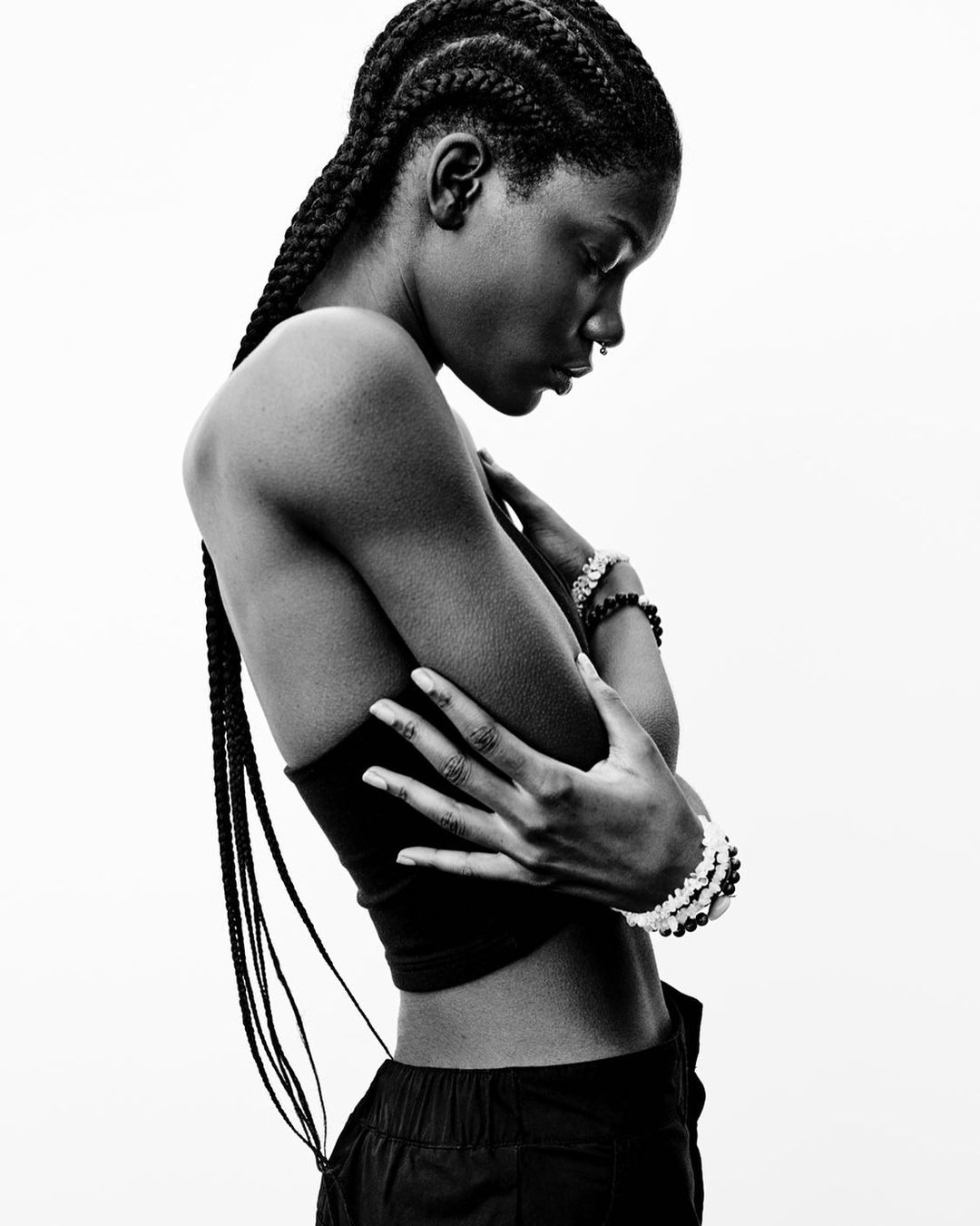 Portrait of a young African-American woman with braided hair, arms crossed, wearing a tube top and pants in a black and white photo studio shot.