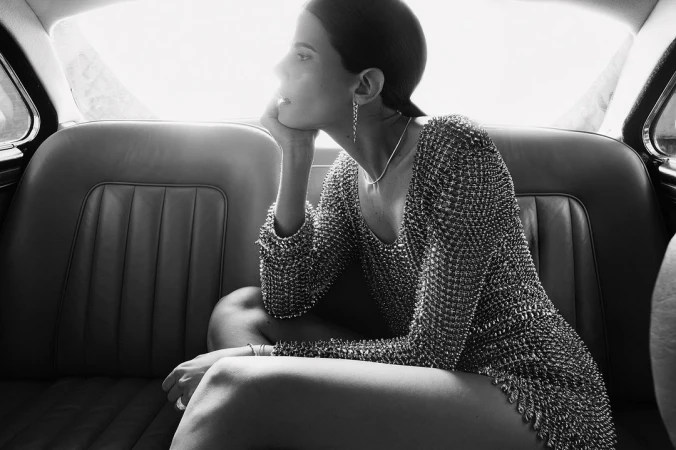 Woman in metallic dress sits in a classic car, black and white. Elegant indoor shot with soft light and thoughtful expression.