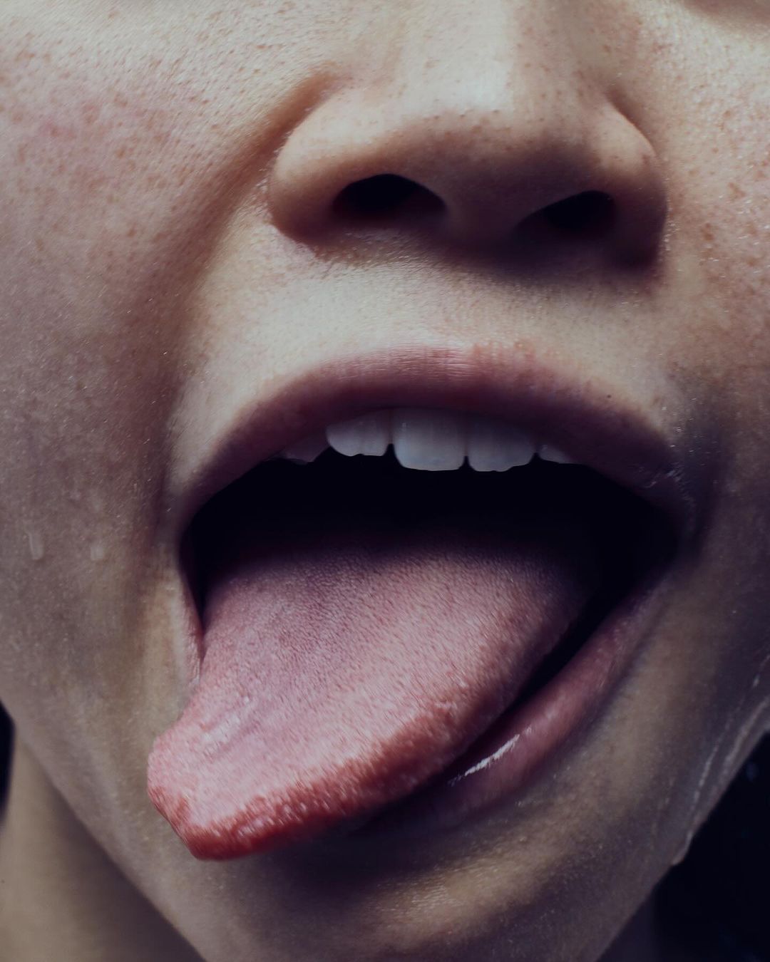 Close-up portrait of a person's face with an open mouth and tongue extended, capturing a raw and intimate moment in a studio setting.