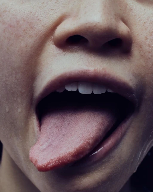 Close-up portrait of a person's face with an open mouth and tongue extended, capturing a raw and intimate moment in a studio setting.