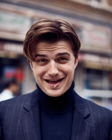 Handsome man in a pinstripe suit smiles with a toothpick in his mouth, portrait shot in front of an urban storefront.