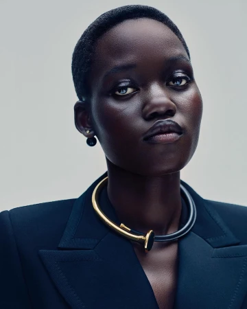 Close-up portrait of a Black woman with short hair wearing a dark blazer and a gold and black collar necklace