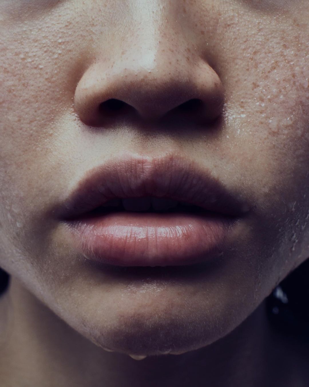 Close-up on an adult female's face. Her skin is damp, and a droplet hangs from her lower lip. The photo has natural lighting.