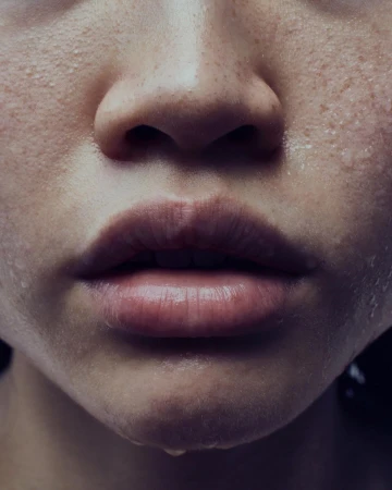 Close-up on an adult female's face. Her skin is damp, and a droplet hangs from her lower lip. The photo has natural lighting.