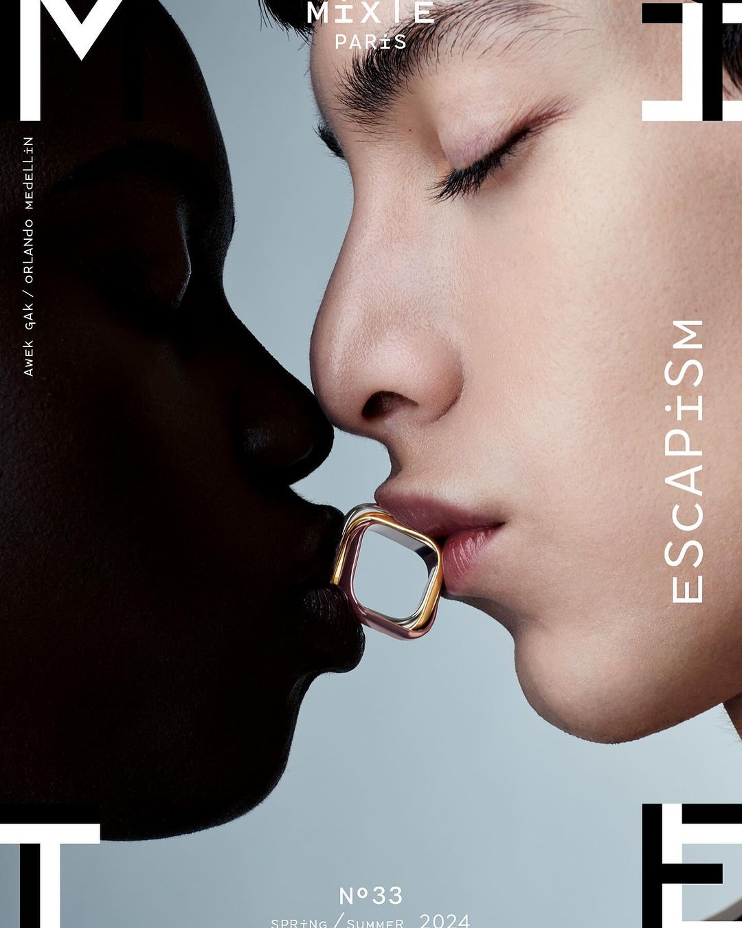 Fashion magazine cover with two faces, one dark-skinned and one light-skinned, touching lips through a cube-shaped lip ring, stylish and modern.