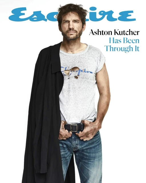 Ashton Kutcher gazes in an Esquire cover shot. He wears jeans, a t-shirt, and a black coat, posing against a plain white backdrop.