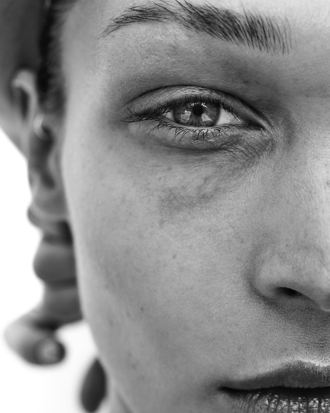 Extreme close-up monochrome portrait of a person's eye and cheek by photographer Billy Kidd against a white background