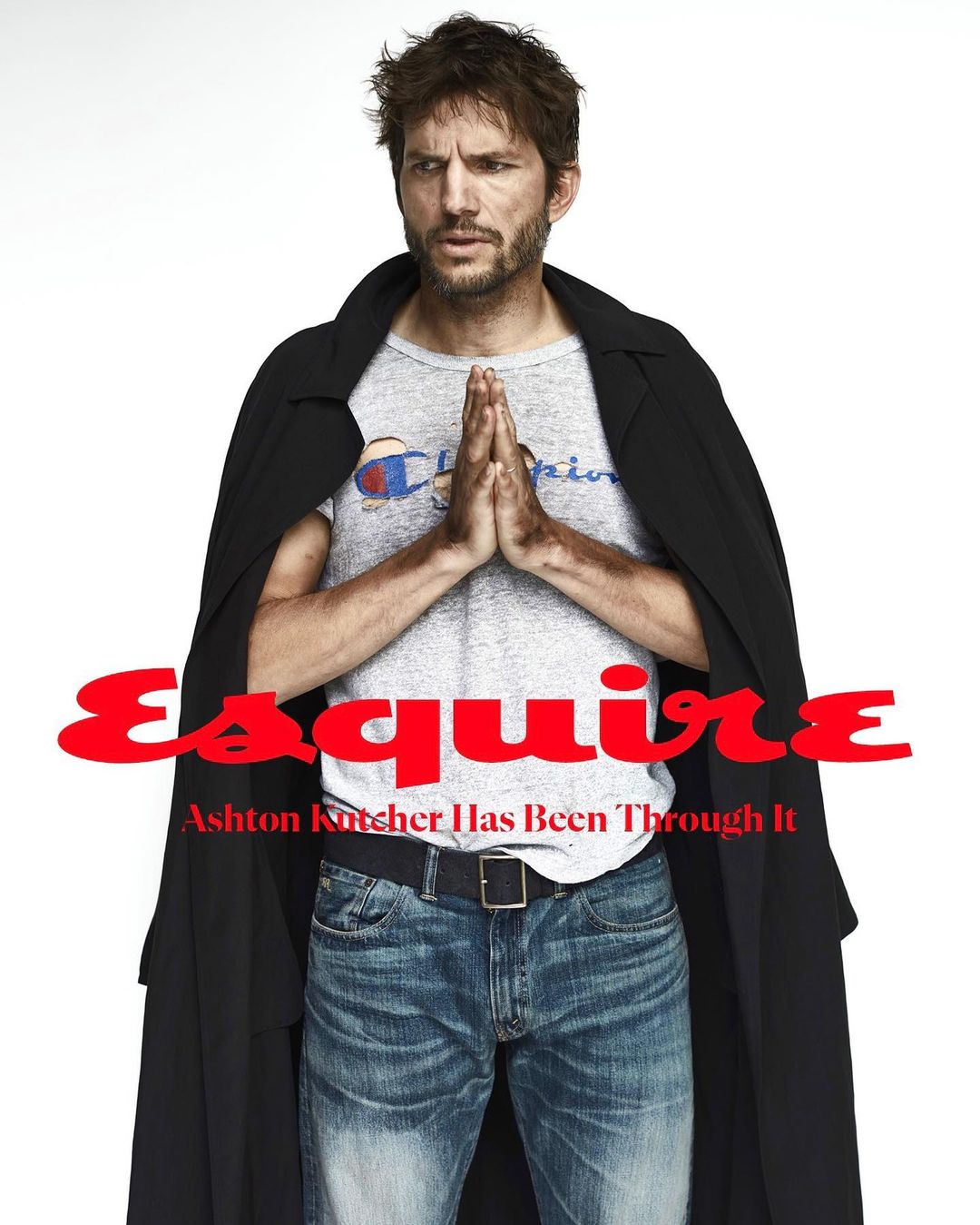 Portrait of Ashton Kutcher wearing a Champion t-shirt, jeans, and black coat with Esquire magazine text overlay on a white background.