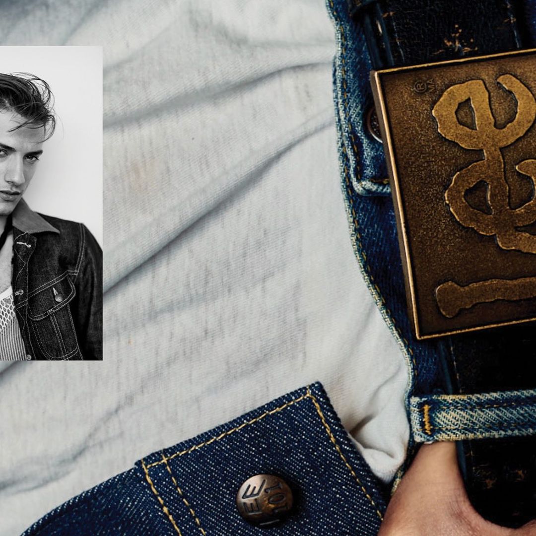 Close-up fashion shot: adult male poses in black and white photo booth-style portrait, wears denim jacket against a washed-out backdrop.