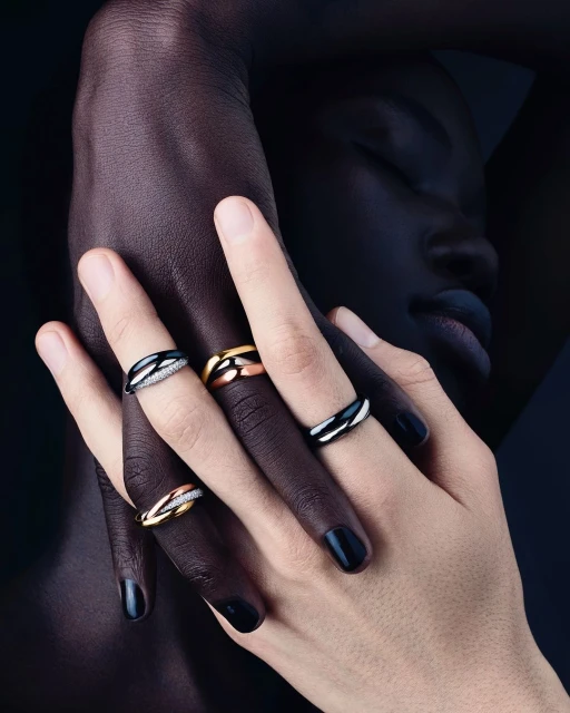 Two adult hands with different skin tones interlocked, each adorned with stylish rings against a dark, dramatic background.