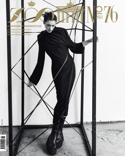 Fashion magazine cover featuring a slender female model in a black dress, posing within a black cube structure against a neutral backdrop.