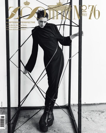 Fashion magazine cover featuring a slender female model in a black dress, posing within a black cube structure against a neutral backdrop.