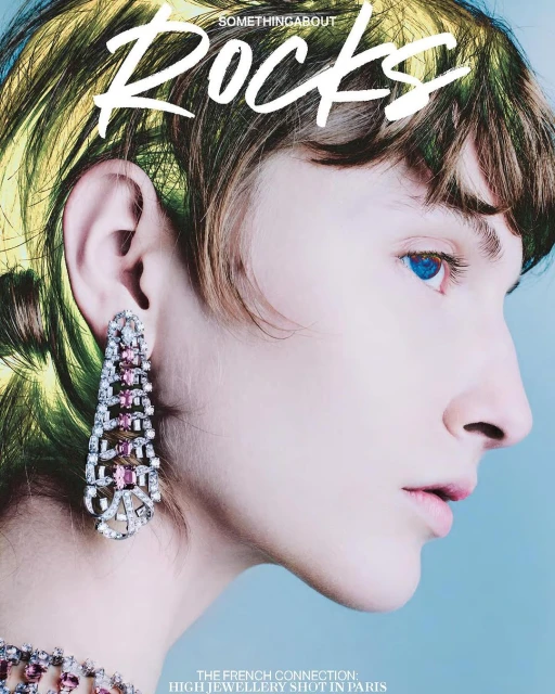 Close-up of a fair-skinned adult female wearing ornate dangling earrings and a matching necklace, against a pale-blue gradient background.