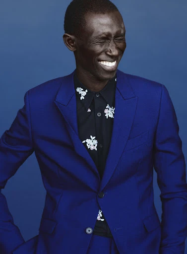 Portrait of adult Black man smiling in blue suit with floral shirt against blue background in studio lighting for fashion editorial.