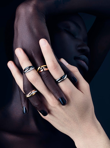 Jewelry ad featuring the interlocked hands of two people with contrasting skin tones displaying interlocking precious metal rings.