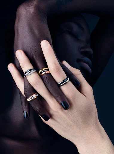 Jewelry ad featuring the interlocked hands of two people with contrasting skin tones displaying interlocking precious metal rings.